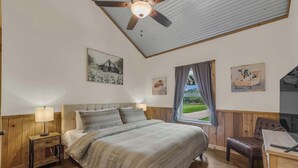 Un dormitorio con una cama, cabecera de madera, mesitas de noche, un escritorio y un ventilador de techo.