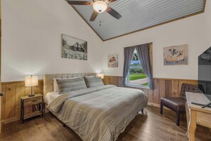 Un dormitorio con una cama, cabecera de madera, mesitas de noche, un escritorio y un ventilador de techo.