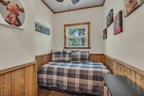 A cozy bedroom with a wooden headboard, a plaid bedspread, and a window with a view of trees.