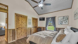 A bedroom with a bed, wooden doors, a ceiling fan, and a window with curtains.