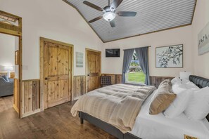 A bedroom with a bed, wooden doors, a ceiling fan, and a window with curtains.