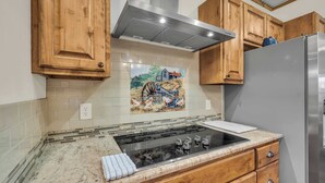 A kitchen with wooden cabinets, a stainless steel refrigerator, and a tiled backsplash with a farm scene.