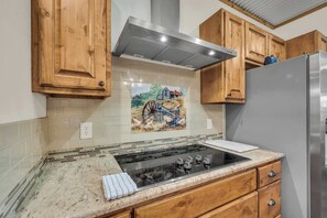 Eine Küche mit Holzausstattung, einem Edelstahlkühlschrank und einer gefliesten Spritzschutzleiste mit einer ländlichen Szene.