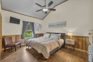 Ein Schlafzimmer mit Bett, einer Holzbank, einem Nachttisch und einem Deckenventilator.