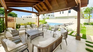 A covered outdoor seating area with a pool in the background. - Family Villa in Punta Cana! Heated Pool (Punta Cana)