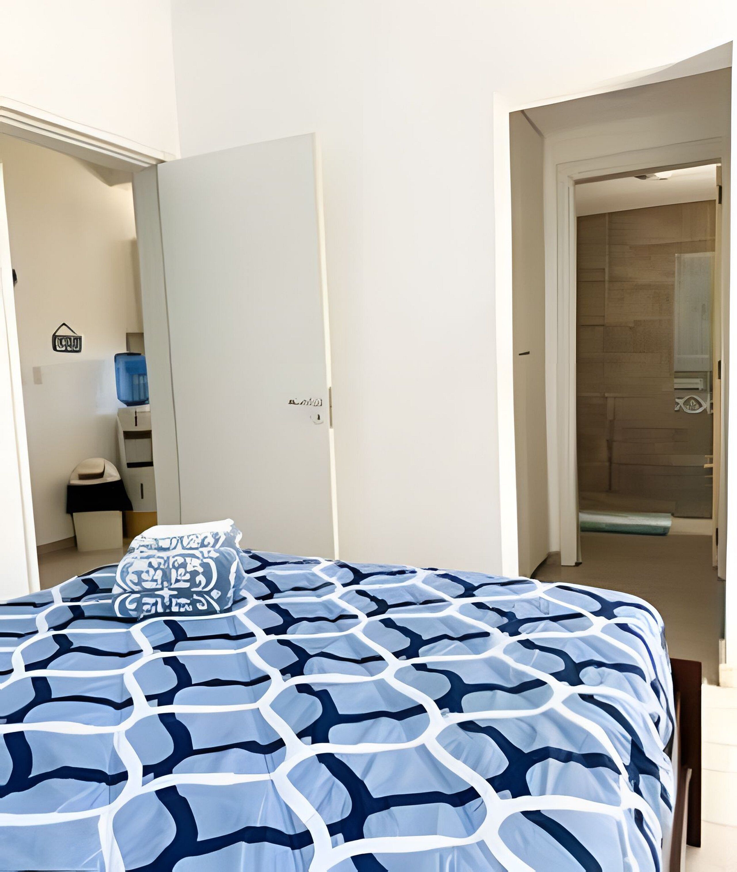 A bedroom with a bed, a nightstand, a lamp, and a door leading to a bathroom.