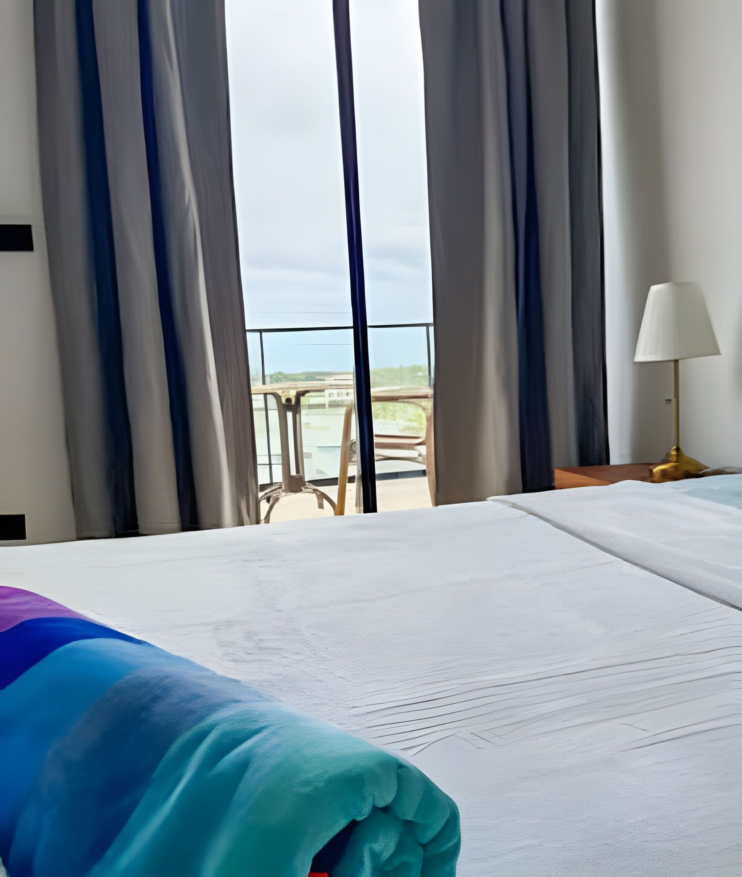 Ein Hotelzimmer mit Bett, Blick auf den Strand und einem Stuhl vor dem Fenster.