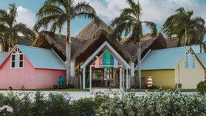 A row of colorful beach cottages with thatched roofs, surrounded by palm trees and cacti. - Incredible Studio in the heart of Punta Cana (Punta Cana)