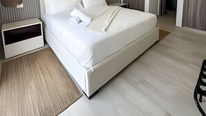 Een moderne hotelkamer met een groot bed, nachtkastjes, een bedlampje, een plafondlamp, een schilderij aan de muur en een deur naar een andere kamer.