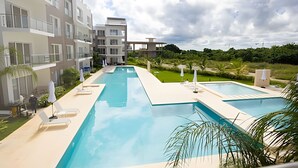 Een modern hotel met een groot buitenzwembad, meerdere balkons en weelderige begroeiing.