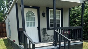 A house with a front porch, a door, a window, and a small outdoor seating area. - Cozy cabin in nice Wylie with AC (Wylie)