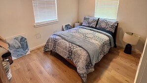 A bedroom with a bed, two windows with blinds, a bedside lamp, and a nightstand. - Cozy cabin in nice Wylie with AC (Wylie)