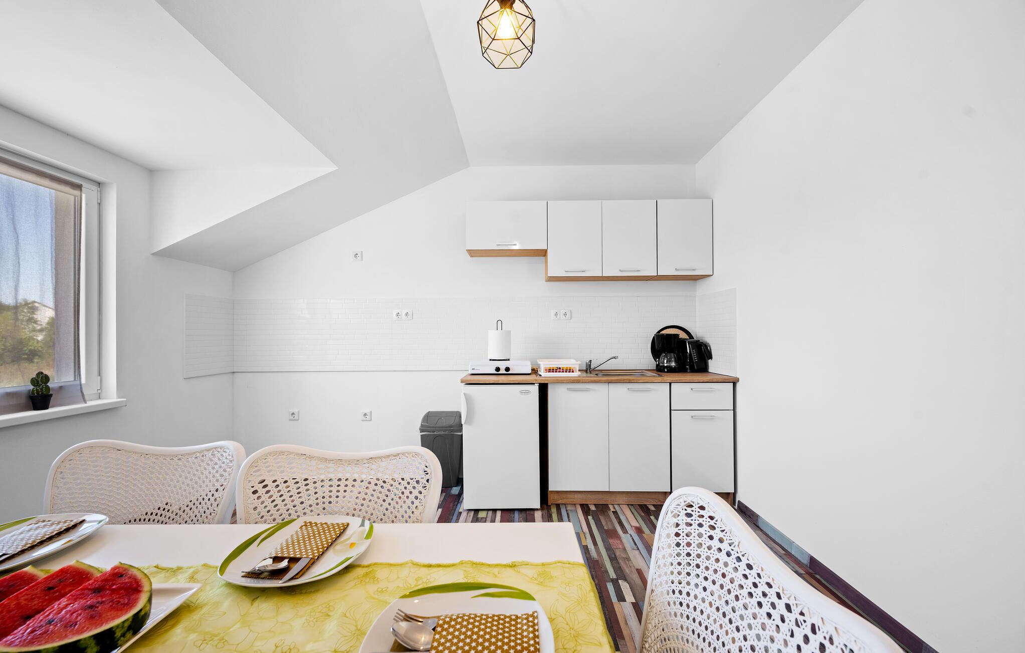 Een moderne keuken met witte kastjes, een eethoek met een tafel voor twee en uitzicht buiten door een raam.