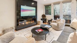 A modern living room with a fireplace, a flat-screen TV, and a large window. - The Ice House: Luxury & Location w/ pool & hot tub (Telluride)