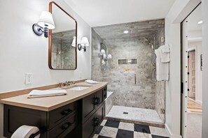 A modern bathroom with a large mirror, two sinks, a shower area, and a checkered floor.