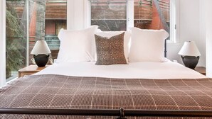 A bedroom with a large bed, two bedside lamps, and a view of a wooden structure outside. - The Ice House: Luxury & Location w/ pool & hot tub (Telluride)