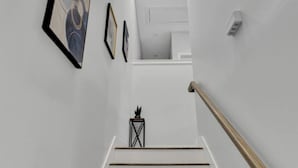Eine Treppe mit Holzgeländer, weißen Wänden und gerahmten Kunstwerken.