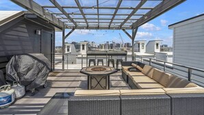 A rooftop patio with a covered seating area, a grill, and a view of the city skyline.