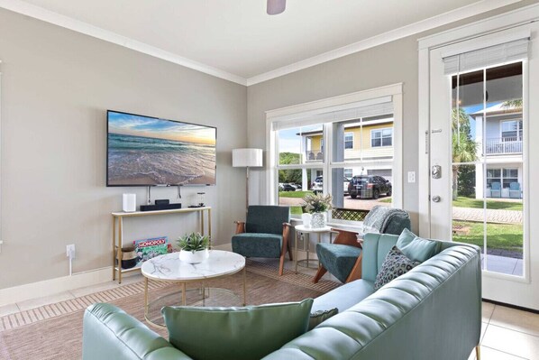A living room with a sofa, chairs, a coffee table, a TV, and a view of a building outside. - Walk to Beach | Golf Cart | Pool | Air Hockey| BBQ (Miramar Beach)