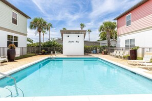 A swimming pool with a sign reading 'Leisure Bay,' surrounded by houses and palm trees.