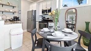A modern kitchen with white cabinets, a stainless steel refrigerator, and a dining area with a round table set for four.