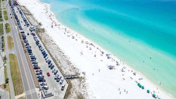 An aerial view of a beach with a parking lot and beachgoers.