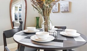 A dining table with white bowls and plates, a vase with dried flowers, and two framed pictures on the wall.