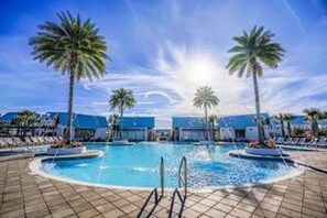Un espace piscine agrémenté de palmiers, de chaises longues et surplombé d’un ciel dégagé.