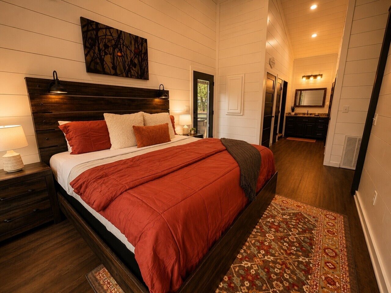 Une chambre à coucher comprenant un grand lit, une table de chevet, une commode, un miroir et une porte donnant sur une autre pièce.