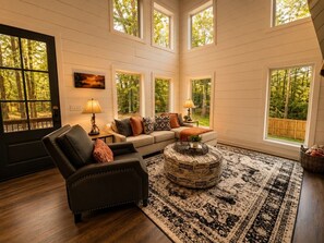 A cozy living room with a sofa, a leather armchair, a round coffee table, and a patterned rug. - 1BR Cabin • HotTub & Fire Pit |BBQ | Patio | Pets (Broken Bow)
