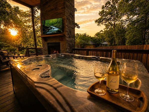 Un bain à remous avec une terrasse en bois, une cheminée et un écran de télévision.