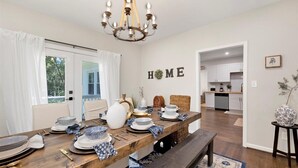 A dining area with a wooden table set for four, a chandelier, and a 'HOME' sign on the wall. - Peaceful Lake House - Sleeps 10, Games, Fishing & Near Downtown/Airport/BJCC (Birmingham)