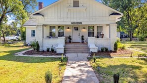 A white two-story house with a front porch, labeled "Lake House," featuring a welcoming entrance, steps, and potted plants. - Peaceful Lake House - Sleeps 10, Games, Fishing & Near Downtown/Airport/BJCC (Birmingham)