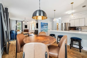 A dining area with a round table, leather chairs, pendant lighting, and a kitchen in the background. - 30A Private Gulf Retreat| Bay Access| Patio | BBQ (Santa Rosa Beach)