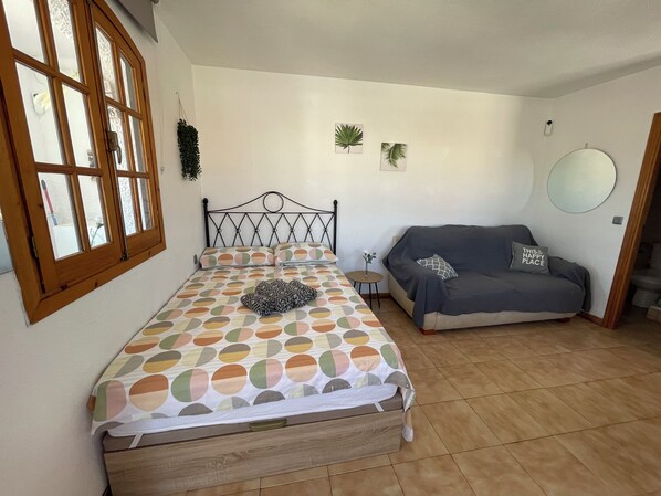 A bedroom with a bed, a sofa, a small table, and a window with curtains. - Mar Menor Studio Cielo - pet-friendly, pool and wi-fi (Cartagena)