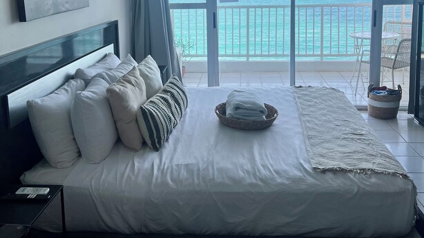 Een slaapkamer met een groot bed, uitzicht op de oceaan en een balkon met een tafel en stoelen.