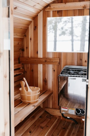 Un sauna en bois avec un banc, un seau en bois et un appareil de chauffage pour sauna portant l'inscription « HARVIA ».