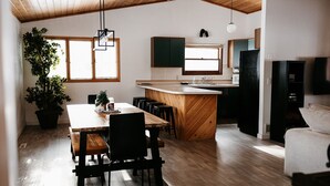 Una cocina moderna con armarios de madera, una isla central y una zona de comedor con mesa y sillas de madera.