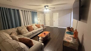 A living room with a sofa, coffee table, and a flat-screen TV mounted on the wall. - Raytown Ranch - Mahome Away from Home (Raytown)