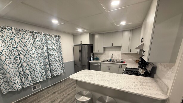 A modern kitchen with a marble countertop, stainless steel appliances, and a bar area with stools. - Raytown Ranch - Mahome Away from Home (Raytown)