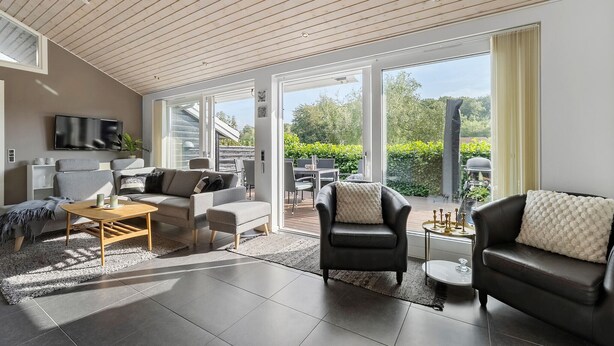 A spacious living room with a large window, a flat-screen TV, and a dining area with outdoor seating. - 3 bedroom amazing home in Slagelse (Slagelse)
