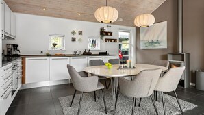 A modern kitchen with white cabinetry, a central island, and a dining area with four chairs. - 3 bedroom amazing home in Slagelse (Slagelse)