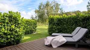 A wooden deck with two lounge chairs and a blanket, surrounded by well-maintained hedges and a grassy lawn. - 3 bedroom amazing home in Slagelse (Slagelse)