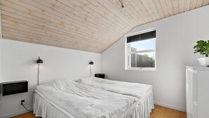 A bedroom with a sloped ceiling, a bed with white bedding, a small bedside table, a wall-mounted TV, and a window with a view of the outside. - 3 bedroom amazing home in Slagelse (Slagelse)