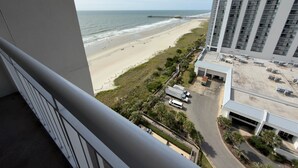A high-rise hotel overlooking a beach with a parking area and a road leading to the beach.