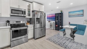 A modern kitchen with stainless steel appliances, white cabinetry, and a seating area with a blue cushion.