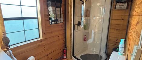 Baño de cabaña de madera con ducha, inodoro y ventana.