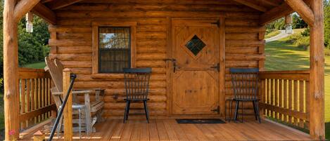 Une cabane en bois avec une véranda, deux chaises, une table et une fenêtre.