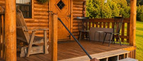Une cabane en bois avec une véranda, une porte dotée d’une fenêtre et une chaise.