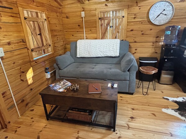 L’intérieur chaleureux d’un chalet avec un canapé gris, une table basse et une horloge au mur.